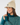 A woman wearing a cream ribbed knit pom-pom beanie with a small circular logo patch and a teal patterned knit golf sweater.