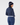 A woman shown from the back wearing a navy blue long-sleeve golf top, matching navy pants with a white belt, and a navy beanie with a cream stripe.
