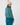 Teal women’s pattern golf sweater with turtleneck and ribbed cuffs, modeled from the back.