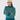A woman wearing a teal and cream patterned knit turtleneck golf sweater, a cream beanie with a pom-pom, and teal pants.