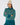A woman wearing a teal and cream patterned knit turtleneck golf sweater, a cream beanie with a pom-pom, and teal pants.