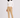 A woman modeling a beige slim-fit golf trousers with white ribbed turtleneck sweater, and white trainers.