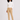 A woman modeling a beige slim-fit golf trousers with white ribbed turtleneck sweater, and white trainers.