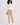 A woman modeling a beige slim-fit golf trousers with white ribbed turtleneck sweater, and white trainers.