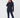 A woman modeling a dark navy blue two-piece tracksuit consisting of a long-sleeve quarter-zip fleece and matching pants, worn over a bright pink shirt, against a plain light gray background.