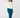 A woman wearing a white long-sleeve crewneck sweatshirt with a small black 'GOLF' with a star logo on the chest, paired with teal pants and teal socks.