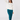 A woman wearing a white long-sleeve crewneck sweatshirt with a small black 'GOLF' with a star logo on the chest, paired with teal pants and teal socks.