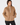 A woman wearing a tan quilted quarter-zip pullover jacket with a stand-up collar and front pockets, paired with black pants, front view.