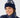 A smiling woman wearing a navy blue knit pom-pom beanie with a white abstract pattern and a matching navy puffer golf jacket.