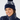 A smiling woman wearing a navy blue knit pom-pom beanie with a white abstract pattern and a matching navy puffer golf jacket.