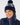 A smiling woman wearing a navy blue knit pom-pom beanie with a white abstract pattern and a matching navy puffer golf jacket.