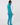 A woman shown from the back wearing a bright turquoise quilted sleeveless golf vest over a white long-sleeve top, matching turquoise pants, and a patterned headband.