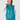 A woman modeling a shiny teal quilted puffer golf vest over a white long-sleeve top and matching teal pants, with a teal patterned headband.