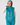 A woman modeling a shiny teal quilted puffer golf vest over a white long-sleeve top and matching teal pants, with a teal patterned headband.