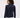 A woman shown from the back wearing a navy blue ribbed mock-neck sweater with contrasting solid shoulder panels, paired with white pants.
