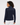A woman shown from the back wearing a navy blue ribbed mock-neck sweater with contrasting solid shoulder panels, paired with white pants.