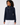 A woman wearing a navy blue ribbed knit sweater with a mock neck and gold zipper detail, paired with white pants.