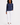 A woman modeling a navy blue long-sleeve golf shirt with a small white 'GOLF' logo on the left chest, paired with white pants and white trainers.