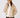 A woman wearing a beige quilted puffer jacket, a tan ribbed knit beanie, a white mock neck top, and dark brown pants.
