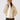 A woman wearing a beige quilted puffer jacket, a tan ribbed knit beanie, a white mock neck top, and dark brown pants.