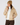 A woman wearing a beige quilted puffer jacket, a tan ribbed knit beanie, a white mock neck top, and dark brown pants.
