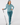 A woman modeling a teal and white patterned long-sleeve button-up shirt, matching teal pants, a headband, and socks, while holding a golf club.