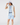 A woman modeling a light blue polo shirt, matching light blue shorts, a white sleeveless zip-front vest, a white bucket hat, and a navy belt.