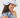 A woman wearing a white wide-brim sun hat with a black embroidered logo and a small blue-and-black strap detail, paired with a light blue ruffled blouse.