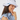 A woman wearing a white wide-brim sun hat with a black embroidered logo and a small blue-and-black strap detail, paired with a light blue ruffled blouse.