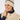 A smiling woman wearing a cream ribbed knit golf beanie with a navy stripe and logo, paired with a matching cream zip-front vest over a navy top.
