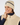 A smiling woman wearing a cream ribbed knit golf beanie with a navy stripe and logo, paired with a matching cream zip-front vest over a navy top.