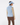 A woman shown from the back wearing a light blue ribbed mock-neck sweater vest over a long-sleeve patterned top, paired with brown pants and a matching light blue visor.