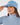 A woman wearing a light blue ribbed knit beanie with a small embroidered logo on the front, paired with a patterned neck gaiter and a matching light blue turtleneck top.