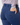 Close-up of a person wearing navy blue tailored trousers, shown from the back with one hand in a back pocket. The person is also wearing a long-sleeve button-up shirt with a multicolor geometric pattern.