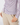 A close-up of a person wearing a long-sleeve button-front top with a white base and a multicolor geometric lattice pattern, paired with light beige trousers.