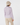 A woman shown from the back wearing a light beige fuzzy bucket hat, a long-sleeve collared shirt with a repeating geometric pattern in white, pink, and purple, and beige trousers.