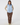 A woman modeling a light blue quilted zip-up vest over a beige patterned long-sleeve top, brown pants, and patterned socks, front view.