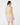 A woman is shown from the back wearing a light beige quilted sleeveless golf puffer vest over a light blue ruffled shirt, paired with a white, purple, and pink patterned mini skirt and a matching patterned headband.