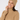 A smiling woman wearing a ribbed knit beige beanie with a small circular star logo patch and a matching beige turtleneck sweater.
