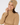 A smiling woman wearing a ribbed knit beige beanie with a small circular star logo patch and a matching beige turtleneck sweater.