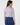 A woman shown from the back wearing a long-sleeve button-up shirt with a small geometric pattern in pink, white, and blue, paired with navy blue trousers.