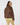 A woman shown from the back wearing a brown sherpa fleece jacket with smooth brown paneling, a patterned headband, and patterned leggings.