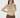 A smiling model wearing a long-sleeve mock neck top with a dense geometric pattern in beige, brown, and yellow, paired with brown pants, against a light gray studio background.
