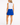 A woman is shown from the back wearing a blue patterned collar and a bright blue golf skort with a small white star logo and text on the back side. Paired with a sleeveless white top and white sneakers.