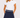 A woman wearing a navy blue golf skort featuring a patterned waistband and gold star details and white short-sleeve polo shirt with ruffled sleeves.