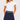 A woman wearing a navy blue golf skort featuring a patterned waistband and gold star details and white short-sleeve polo shirt with ruffled sleeves.