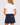 A woman shown from the back wearing a navy blue A-line golf skort with white decorative trim and a small embroidered star paired with a white short-sleeve ruffled blouse.