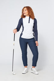 Model wearing the white and navy blue long sleeve polo shirt paired with matching navy blue pants, posing with a golf club.